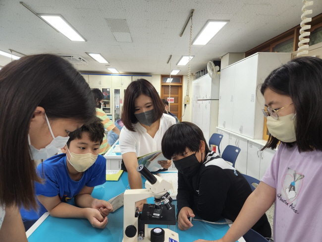 지난 7월 경기 시흥시 월포초 과학실에서 5학년 2반 친구들이 모란(가운데) 교사의 지도 아래 현미경 구조와 원생물에 대해 배우고 있다.  초록우산어린이재단 제공