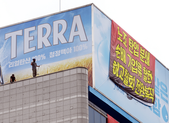 민주노총 공공운수노조 화물연대 조합원 70여 명이 16일 오전 서울 강남구 청담동 하이트진로 본사를 불법 점거한 가운데, 옥상에서 농성 중인 한 조합원이 외벽 꼭대기에 올라 구호를 외치고 있다. 윤성호 기자