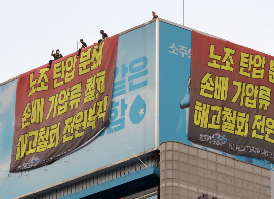 지난 16일부터 하이트진로 본사 옥상에서 고공농성을 하고 있는 민주노총 화물연대 조합원들이 18일 오후 서울 강남구 하이트진로 본사 앞에서 열린 ‘고공농성 투쟁 승리 결의대회’를 지켜보고 있다. 뉴시스