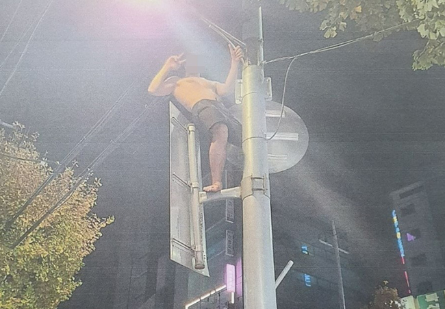 ‘신림동 타잔’으로 통했던 A(33) 씨가 지난 15일 오전 5시쯤 서울 관악구 신림동에서 행인을 소주병 등으로 위협한 뒤 가로등에 올라가 ‘브이’ 포즈를 취하고 있다. 제보자 제공