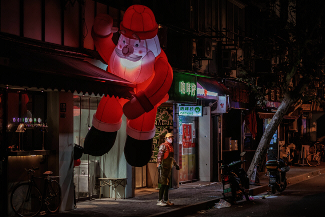 17일 중국 상하이에서 크리스마스를 기념하기 위한 산타 풍선이 장식된 식당 앞에 한 여성이 홀로 우두커니 서 있다. 중국 정부가 ‘제로 코로나’ 정책을 해제했지만 비공식 확진자가 폭증하자 중국인들이 외출을 자제하면서 연말에도 거리가 한산하다.  EPA 연합뉴스