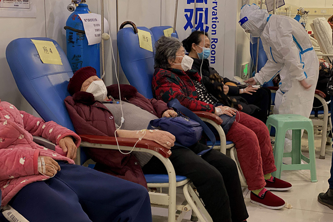 지난 23일(현지시간) 중국 남서부 충칭시 충칭의과대학 제2부속병원에서 코로나19 환자들이 팔에 주사를 꽂은 채 줄지어 앉아있다. AFP 연합뉴스