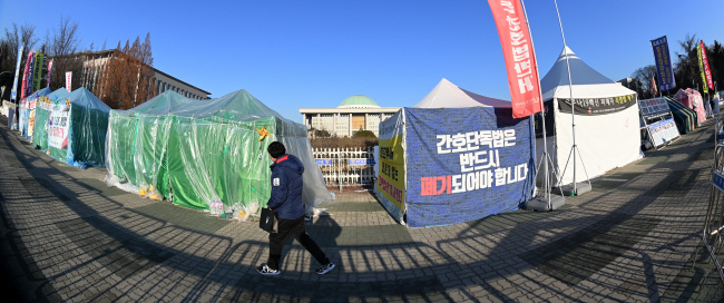 4일 오전 한 시민이 서울 영등포구 국회의사당 앞 인도에 설치된 민주노총 등 각종 단체의 불법 천막 앞을 지나가고 있다. 천막·텐트의 난립으로 10m 이상 넉넉한 폭의 인도가 절반으로 줄어들어 여의도 직장인 등이 큰 불편을 겪고 있다.  문호남 기자