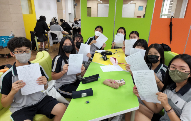 인천 부평구 진산중학교 학생들이 지난해 학교 도서관에서 좋아하는 책 한 페이지를 필사하는 ‘예쁜 손글씨 쓰기 대회’에 참여한 뒤 직접 쓴 손글씨 종이를 들어보이고 있다. 초록우산어린이재단 제공