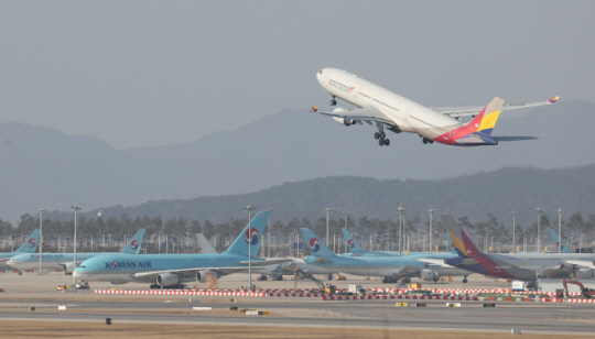 지난 12일 대한항공 여객기들이 세워져 있는 인천국제공항 활주로에서 아시아나항공 여객기 한 대가 이륙하고 있다. 연합뉴스