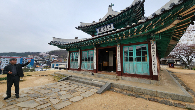 한옥 구조의 강화성당에 대해 이경래 신부가 설명하고 있다. 왼쪽으로 강화읍이 보이고, 오른쪽 마당에 불교 상징인 보리수가 있다.