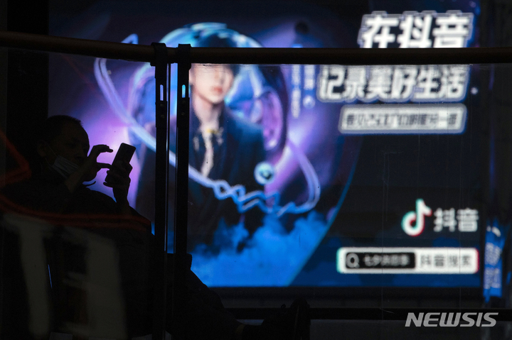 [베이징=AP/뉴시스]2020년 8월30일 베이징의 한 쇼핑몰에서 틱톡의 중국 자매 앱인 더우인 (抖音)광고 앞에 스마트폰을 사용하는 한 남성이 서 있다. 더우인에서 과도한 술을 마시는 모습을 생중계하던 사람이 숨져 중국 사회에 거센 분노를 촉발하고, 동영상 사이트들에 대한 엄격한 규제를 촉구하는 목소리가 높아지고 있다고 BBC가 11일 보도했다. 2023.05.22.