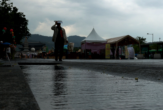 비가 내린 지난 18일 오후 서울 세종대로 광화문광장에서 한 시민이 머리를 가린 채 이동하고 있다. 연합뉴스