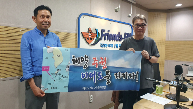 양태룡(왼쪽) 대표가 지난달 16일 국군의 방송에 출연해 원종배 아나운서와 ‘이어도 지키기’ 현수막을 펼쳐 보이고 있다.  양태룡 대표 제공