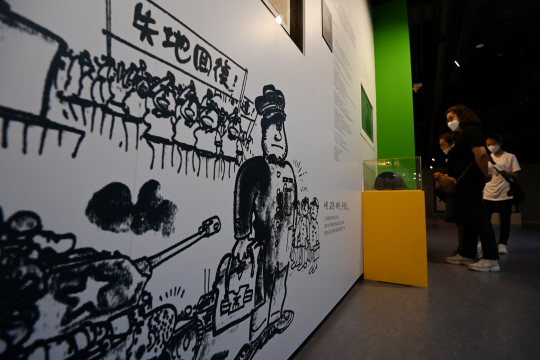 서울 서대문구 대한민국임시정부기념관에서 열린 ’고난 속에 피어난 기적, 피난시절 천막교실‘ 전시에서 시민들이 교복 대신 군복을 입은 학생 그림과 재동초등학교에서 발견된 철모 등을 살펴보고 있다. 문호남 기자