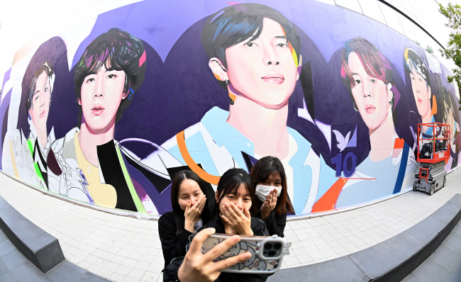 그룹 방탄소년단(BTS)의 데뷔 10주년을 맞아 한국을 찾은 외국인 관광객들이 13일 오전 서울 용산구 하이브 사옥 외벽에 작업 중인 BTS 대형 벽화 앞에서 기념사진을 찍고 있다.   백동현 기자