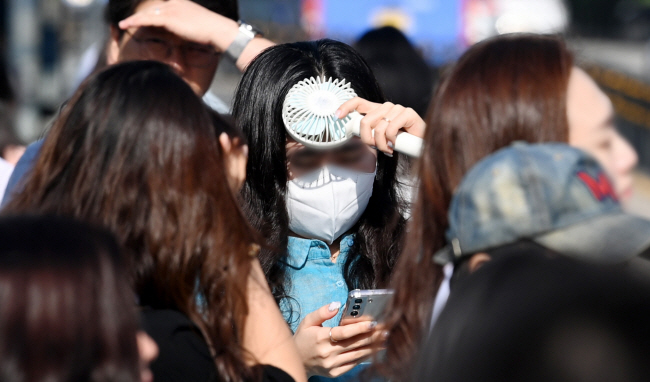 한낮 체감온도가 35도 안팎까지 치솟는 덥고 습한 무더위가 이어지고 있는 가운데 28일 오전 서울 광화문에서 시민들이 휴대용 선풍기 등으로 햇볕을 가리며 출근하고 있다.  윤성호 기자