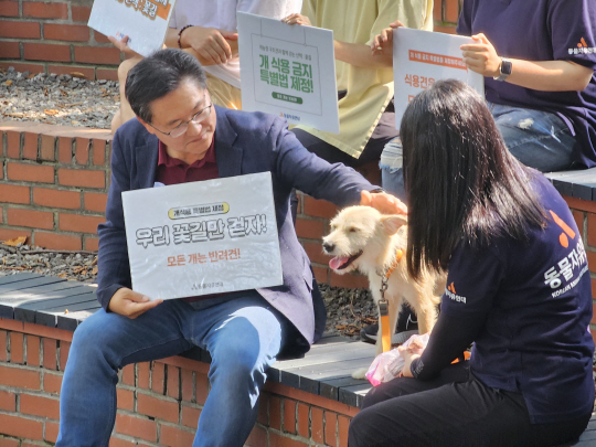 ‘개 식용 금지법’을 발의한 이헌승 국민의힘 의원이 19일 동물자유연대와 함께 국회도서관 야외음악당에서 개최한 ‘개 농장 구조견과 함께 하는 산책 : 꽃길’ 행사에서 참석한 강아지를 쓰다듬고 있다. 이 의원실 제공.