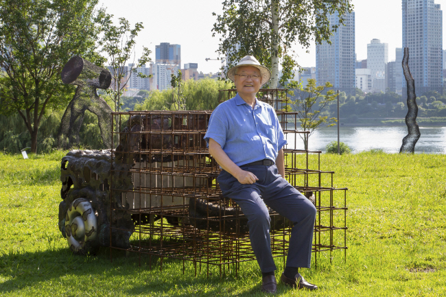 윤영달 크라운해태제과 회장이 ‘2023한강조각프로젝트’에 전시된 홍경태 작가의 작품 ‘기억의 단서’에 걸터앉아 미소 짓고 있다.  크라운해태 제공