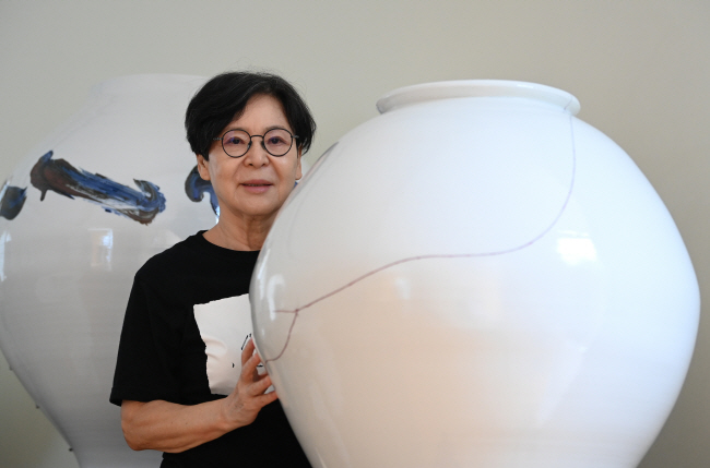 박영숙 도예가가 경기 성남시에 위치한 작업실에 놓인 백자 달항아리와 함께 서있다. 이 백자는 깨진 것을 옻칠로 이어 붙여 복원한 작품이다. 박윤슬 기자