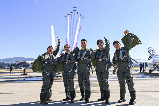 국민조종사와 명예조종사가 21일 공군 서울공항에서 국산 초음속 고등훈련기 T-50 체험비행에 앞서 블랙이글스 비행을 배경으로 기념촬영을 하고 있다. 왼쪽부터 미셸 장, 이호정, 김종섭, 김의현, 유동현씨. 공군 제공