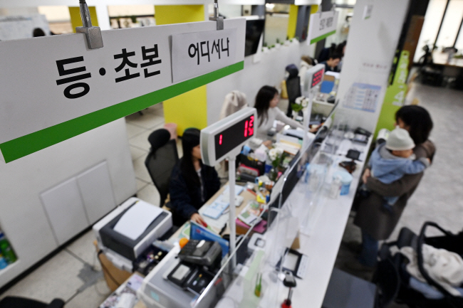23일 오전 서울 종로구 청운효자동주민센터에서 아이를 안은 한 시민이 주민등록등본을 받기 위해 서류를 작성하고 있다. 정부 행정 전산망이 복구된 지 이틀 만인 22일 주민등록시스템이 또 장애를 일으켜 주민등록 증명서 발급 업무가 잠시 지연되는 등 불안한 상황이 계속되고 있다.   백동현 기자