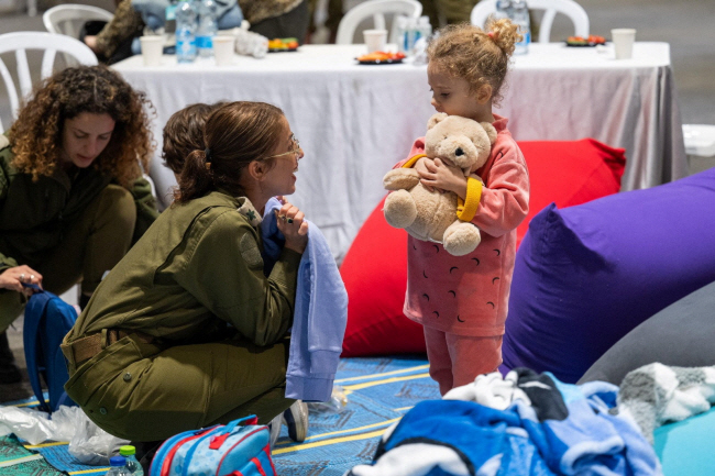 이스라엘과 하마스 간 휴전 이틀째인 25일 하마스로부터 석방된 인질 중 한 명인 야헬 쇼함(3·오른쪽)이 건강검진을 위해 머물고 있는 병원에서 곰 인형을 들고 군인의 이야기를 듣고 있다.   로이터 연합뉴스