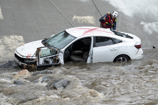 21일(현지시간) 미국 캘리포니아주 노스 힐스에서 경찰, 소방, 수상구조대원들이 물살에 휩쓸려가는 차량을 견인하고 있다. 미 기상청(NWS)은 전날 로스앤젤레스(LA)를 포함한 캘리포니아주 남부 지역 대부분에 겨울 폭우를 예보하며 홍수 경계령을 발령했다. AP 연합뉴스