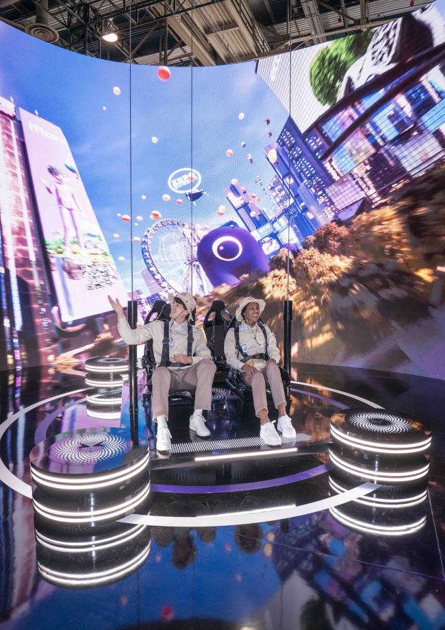 세계 최대 가전·정보기술(IT) 전시회 ‘소비자가전쇼(CES) 2024’의 SK그룹 전시관에서 모델들이 확장현실(XR) 기술로 도심항공교통(UAM)을 체험하도록 한 ‘매직 카펫’을 타고 있다.  SK텔레콤 제공