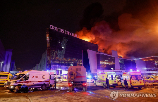 22일(현지시간) 무차별 총격 사건이 벌어진 러시아 모스크바 외곽 대형 콘서트장에서 화염이 치솟고 있다. 외부에는 구급차가 부상자를 이송하기 위해 대기 중이다. 연합뉴스.