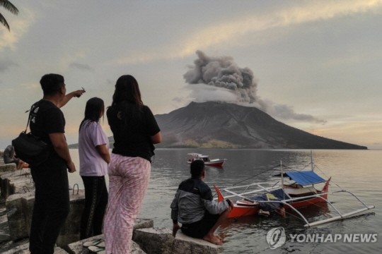 19일 인도네시아 북술라웨시주 타구란당섬 시타로에서 사람들이 바다 건너 루앙 화산의 분화 장면을 지켜보고 있다.   AFP연합뉴스