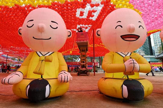 불기 2568년 부처님 오신 날(5월15일)을 앞둔 21일 서울 종로구 조계사에 설치된 스님 조형물 뒤로 관계자가 오색연등에 소원지를 달고 있다. 문호남 기자