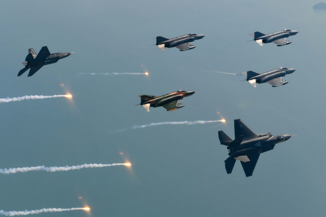 지난 9일 전남 고흥 상공에서 할아버지뻘인 F-4 팬텀 편대 좌우측 꼭짓점에서 비행하던 손자뻘인 국산 초음속 전투기 KF-21 보라매 시제기 2기가 편대에서 떨어져 나오는 ‘피치아웃’ 비행을 하고 있다. F-4 편대는 고별인사를 건네듯 플레어를 사출했다. 공군 제공