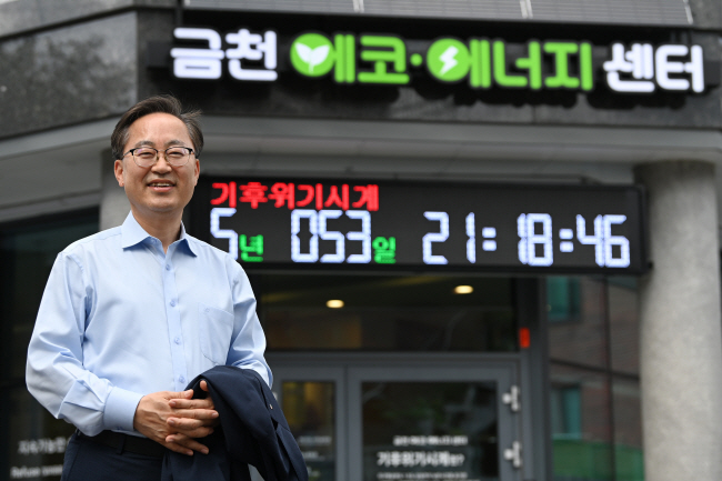 유성훈 서울 금천구청장이 24일 독산1동 금하마을에 있는 ‘금천 에코·에너지센터’ 앞에서 포즈를 취하고 있다. 뒤에 있는 기후위기 시계는 이 센터 정문 위에 설치된 것으로 지구 온도가 산업화 이전 시기보다 1.5도 오르는 시점까지 얼마나 남았는지를 나타낸다. 문호남 기자