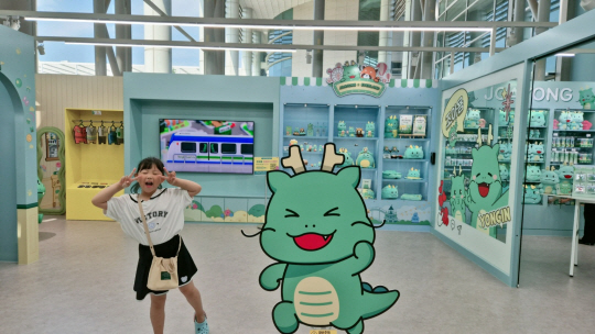 16일 경기 용인시청 1층 민원창구 앞에 마련된 ‘조아용 홍보관’에서 꼬마 손님 소은유(7) 양이 조아용 그림 옆에서 익살스런 표정을 짓고 있다. 용인=박성훈 기자