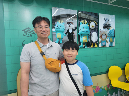 16일 경기 용인시청 1층 민원창구 앞에 마련된 ‘조아용 홍보관’ 내 상품 판매점에서 방문객 성원준(45) 씨와 아들 시헌(10·오른쪽) 군이 용인시 대표 캐릭터인 ‘조아용’과 삼성전자 ‘달수’ EBS ‘팽수’ 에버랜드 ‘레시’ 등 캐릭터가 함께 찍힌 사진 앞에서 활짝 웃고 있다. 용인=박성훈 기자