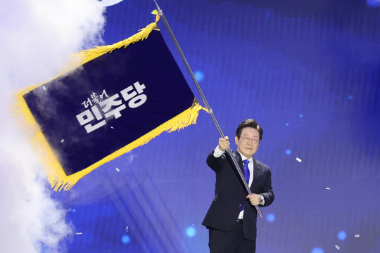 더불어민주당 당대표 연임에 성공한 이재명 신임 당대표가 18일 오후 서울 송파구 올림픽공원 KSPO돔에서 열린 전국당원대회에서 박찬대 대표 직무대행 겸 원내대표로부터 전달받은 당기를 흔들고 있다. 연합뉴스