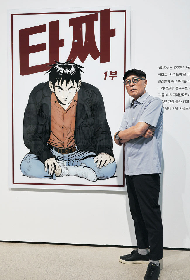 허영만 작가가 영화로도 제작된 만화 원작 ‘타짜’의 포스터 앞에 서 있다. 전남도립미술관 제공