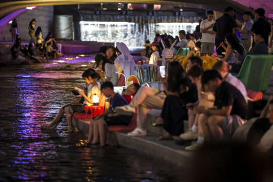 역대 최장 연속 열대야가 이어진 지난 23일 오후 서울 중구 청계천을 찾은 시민들이 휴식을 취하며 더위를 식히고 있다. 뉴시스