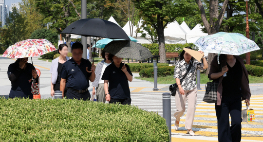 가을 폭염이 기승을 부린 지난 11일 서울 여의도 국회에서 시민들이 양산을 쓰고 이동하고 있다. 뉴시스