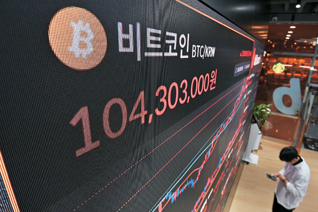 6일 미국 뉴욕증권거래소(NYSE)에서 한 트레이더가 지난 7월 총기 피격 직후 지지자들에게 주먹을 들어 보이던 도널드 트럼프 대통령 당선인의 모습이 인쇄된 티셔츠를 뽐내고 있다(위 사진). 아래 사진은 7일 트럼프 당선인의 승리 소식에 서울 서초구 빗썸라운지 강남점 현황판에 비트코인 가격이 1억 원대를 돌파한 모습. AFP 연합뉴스 백동현 기자