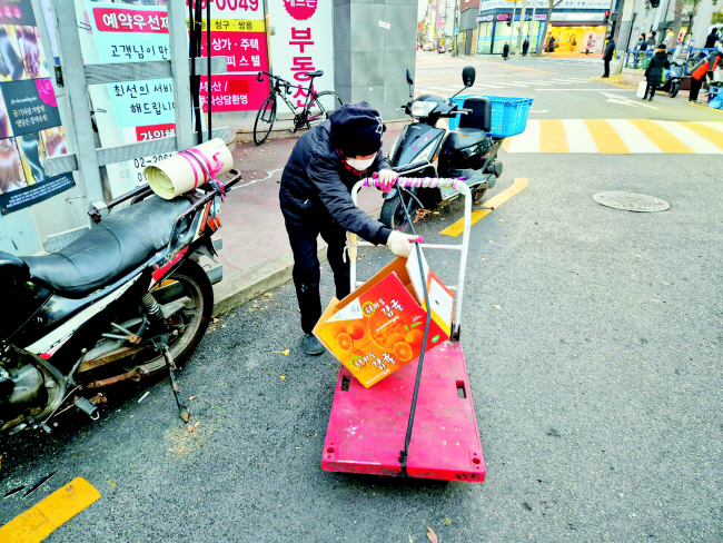 지난 3일 오후 5시쯤 서울 양천구 한 골목에서 폐지수집 노인 홍모(83) 씨가 상가 앞에 버려진 빈 감귤 박스를 발견해 수레에 싣고 있다.   노수빈 기자