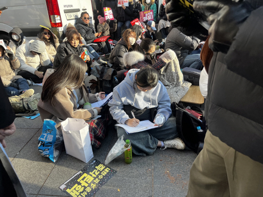 14일 서울 영등포구 여의도 국회 앞에서 열린 ‘탄핵 집회’에서 대학생 정윤주(21) 씨가 응원봉을 들고 집회에 참여하다 대학 기말고사 공부를 하고 있다. 이시영 기자.