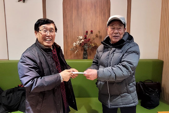 지난 22일 상현교회 카페에서 이영소(왼쪽) 안수집사가 화북초교 동창에게 17일 모금한 120만 원을 전달하고 있다.
