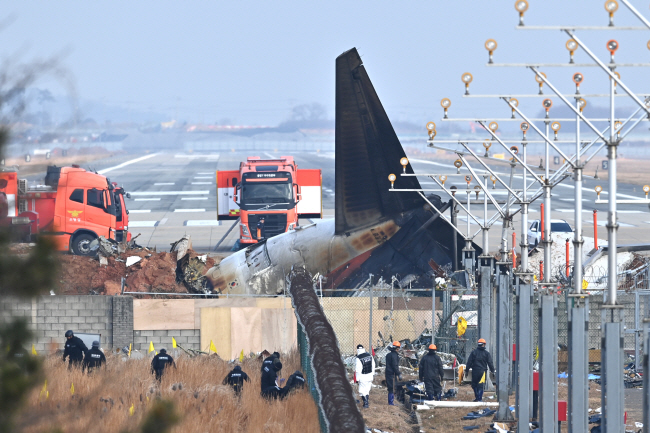 ‘12·29 무안공항 제주항공 참사’ 이튿날인 30일 오전 전남 무안공항 활주로 인근에서 경찰이 유품 수색작업을 하고 있다. 여객기 잔해 뒤로 보이는 활주로에는 동체가 착륙할 때 발생한 마찰 흔적이 보이지 않는다. 백동현 기자