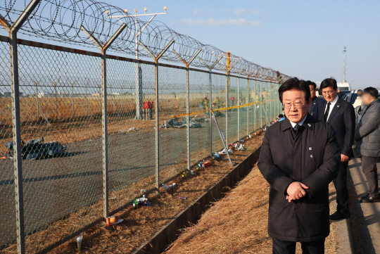 이재명 더불어민주당 대표가 1일 오후 전남 무안군 무안국제공항 제주항공 여객기 참사 현장 외곽 울타리에서 수색 현장과 시민들이 남긴 추모 물품을 보고 있다. 연합뉴스