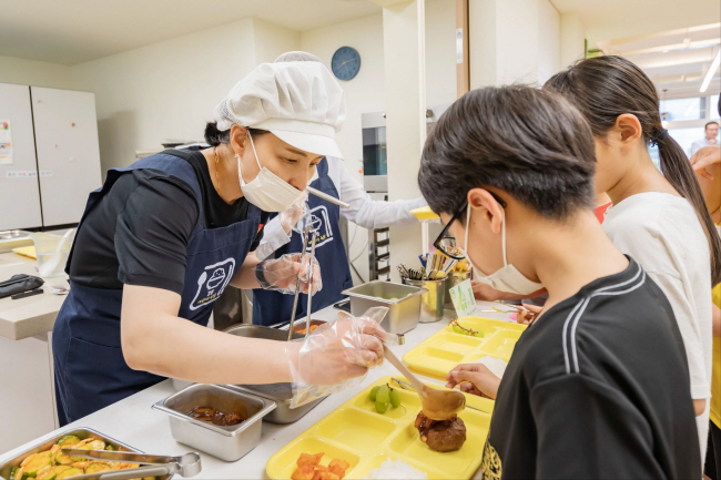 서울 강동구 암사동 강동어린이식당에서 아이들이 이수희 강동구청장이 배식하는 음식을 식판에 받고 있다. 강동구청 제공