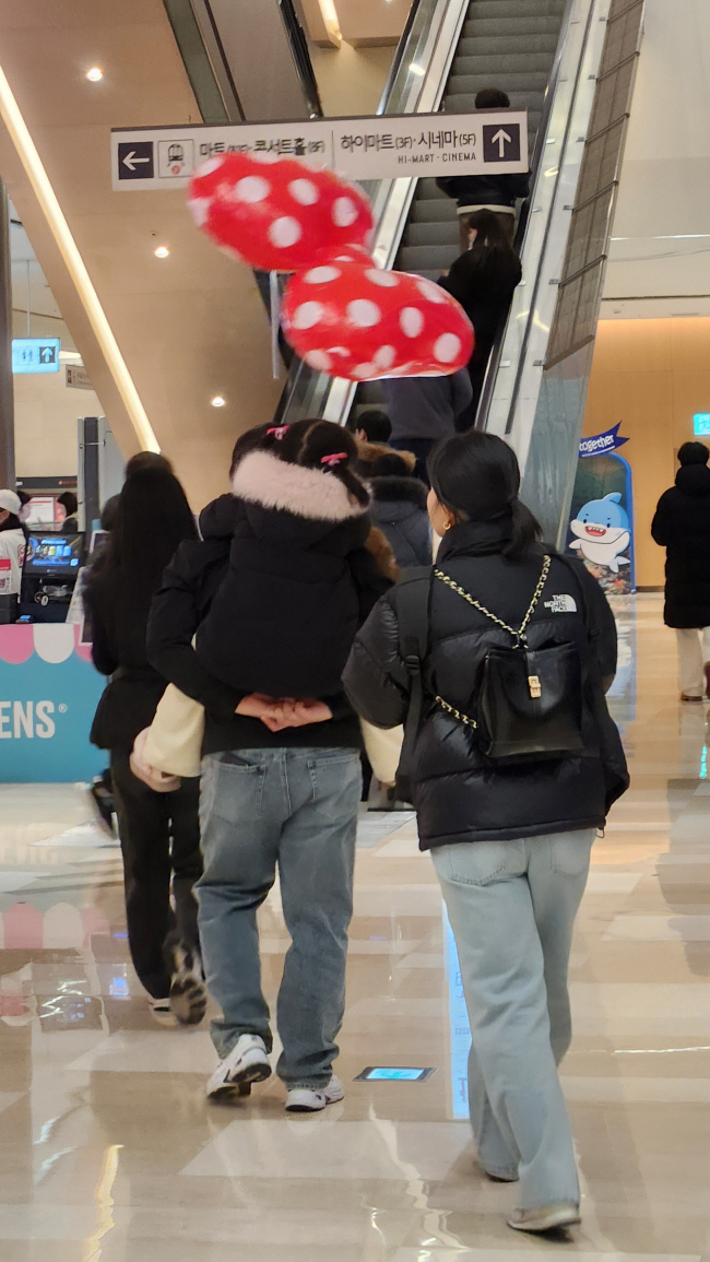 자기 몸집만 한 풍선을 들고 있는 아이를 업은 어느 아빠의 뒷모습.