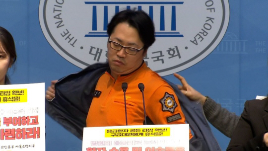 김성현 전국공무원노조 서울소방지부 구급국장이 17일 국회의원회관에서 열린 기자회견에서 "구급대원의 입장으로 이 자리에 서겠다"며 노조 조끼를 벗고 있다. TV조선 방송 캡쳐