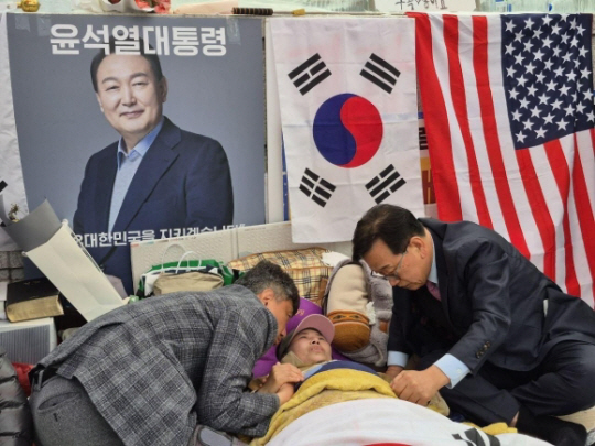 윤석열 대통령 변호인단 소속 석동현(오른쪽) 변호사가 25일 헌법재판소 앞에서 탄핵 반대 단식 시위를 28일째 이어가고 있는 전지영 국가정의실천연합 사무국장을 찾아 손을 잡고 있다. 대통령 변호인단 제공