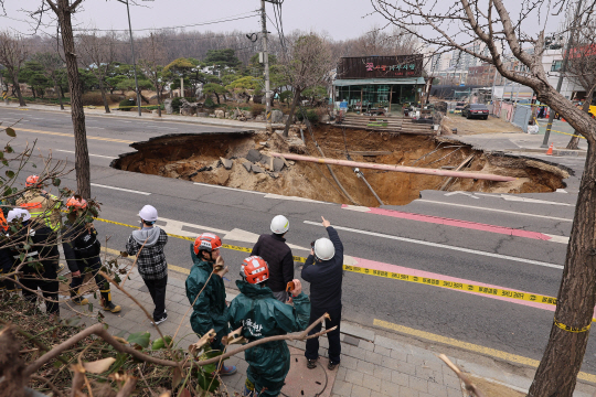 25일 강동구 대명초등학교 앞 도로에서 전날 발생한 대형 땅꺼짐으로 지름 20m, 깊이 18m가량의 대형 싱크홀이 발생한 가운데 관계자들이 관련대책을 논의하고 있다. 연합뉴스
